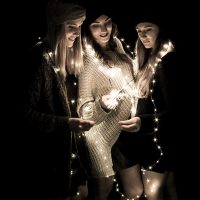 Drei junge Frauen im Dunkeln mit Lichterkette