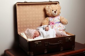 frisch geborenes Baby liegt mit einem teddy in einem ausgepolsterten Koffer, schläft