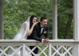 Brautpaar auf hölzerner Terrasse, aneinander geschmiegt, verträumter Blick in die Ferne