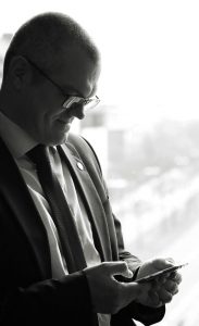 Businessfototgrafie eines Mannes, vor sich hin schmunzelnd, im anzug da stehend und auf sein Handy schauend, schwarzweiß-fotografie