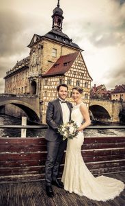 Hochzeitsaar steht in Bamberg auf einer Brücke, das alte Rathaus im Hintergrund