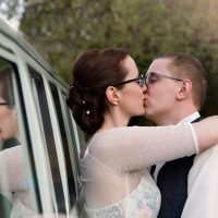 Hochzeitspaar küsst sich, lehnt dabei an altem VW-Bus