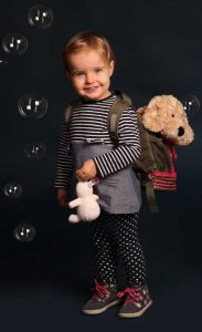 Portraitfoto eines Kleinindes in Seifenblasen eingehüllt, mit Rucksack auf dem Rücken in welchem eine teddy steckt