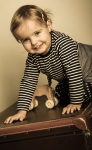 Portraitfoto eines Kleinkindes welches auf einem Koffer krabbelt und lächelt