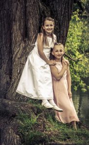 Portraitfoto von zwei jungen Mädchen die in schicken weißen Kleidern im Wlad stehen und lächen