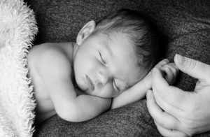 Babyshooting: schlafendes Baby, mit Hand der Eltern in seiner, schwarzweißfoto