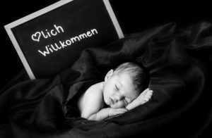 Babyshooting, Baby schläft, liegt eingehüllt in Decken, hinter ihm liegt eine Tafel die mit Herzlich willkommen beschrieben ist